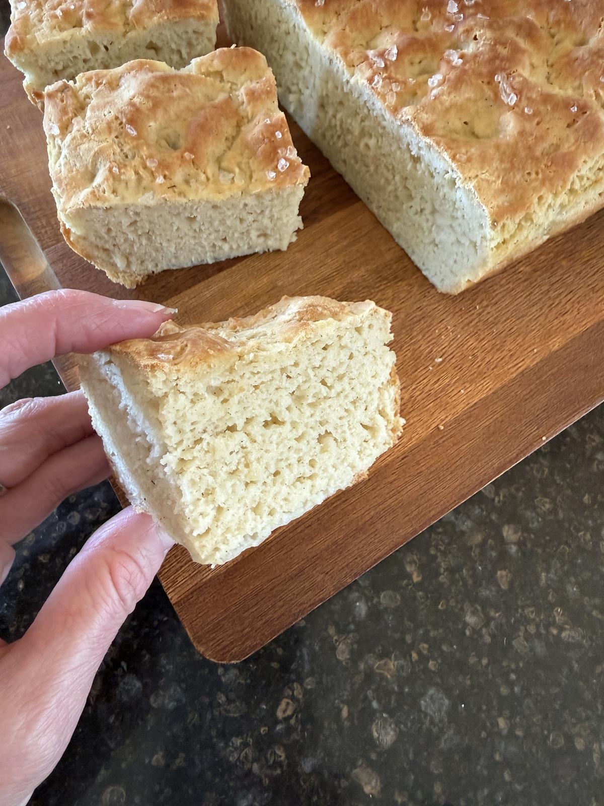 Gluten Free Sourdough Focaccia piece with more bread in background on cutting board