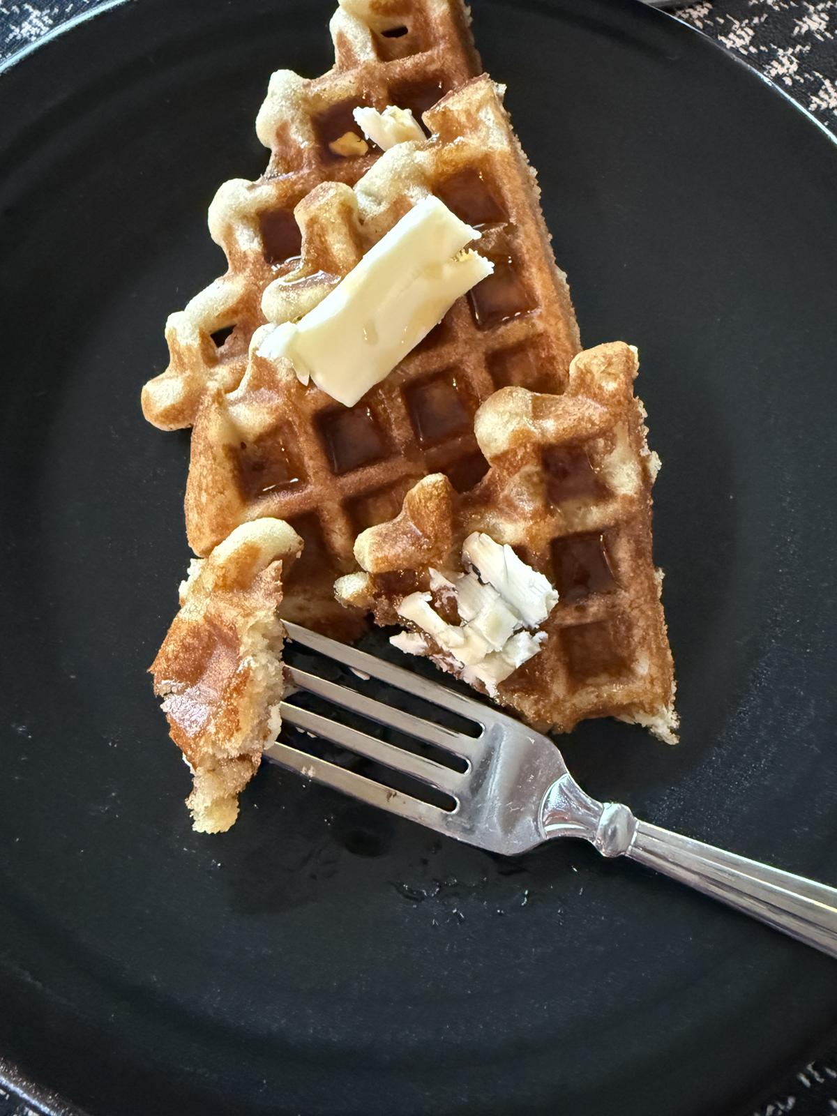 gluten free sourdough waffles on a black plate with butter and syrup