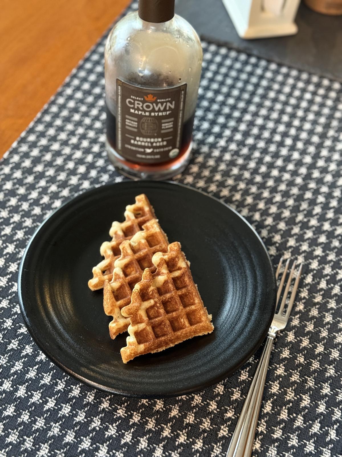 waffles on a black plate with a bottle of syrup in the background