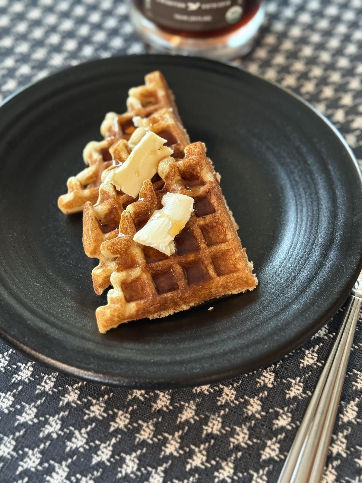 sourdough gluten free waffles with butter and syrup with a fork next to black plate