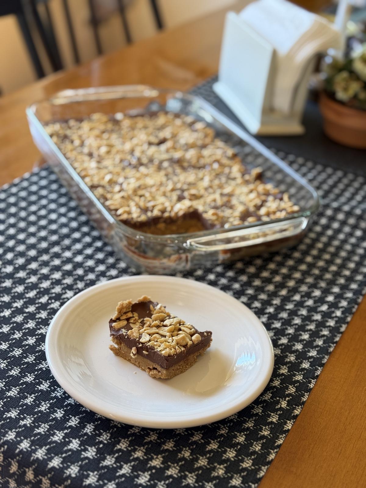 No Bake Peanut Butter Bars in glass pan on black and white table runner with a bar on white plate in front