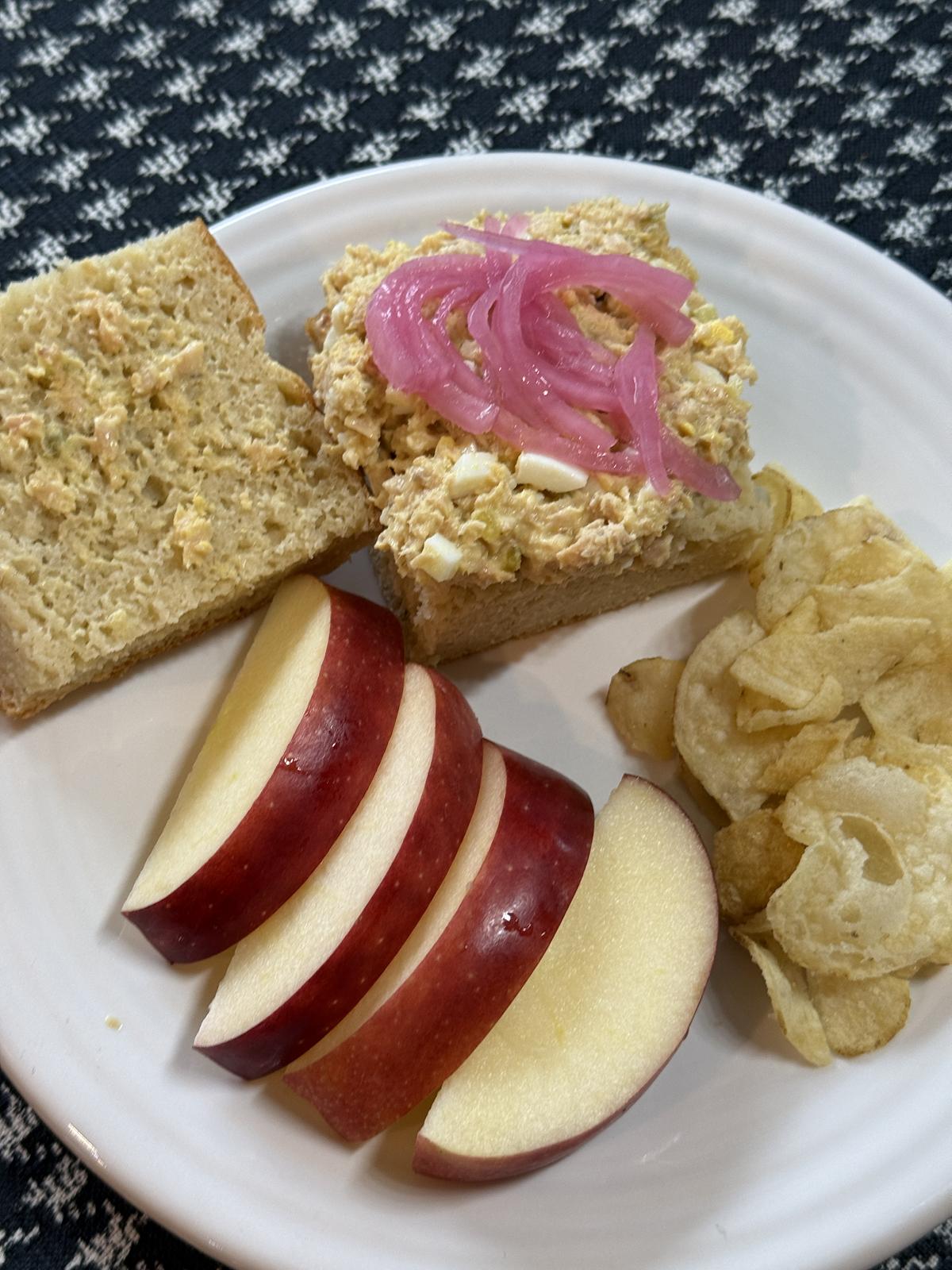 salmon salad sandwich on gluten free focaccia with pickled onions and apples and chips on a white plate