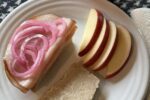 pickled onions on a turkey sandwich on white plate with apples