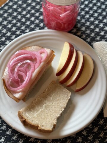 pickled onions on a turkey sandwich on white plate with apples