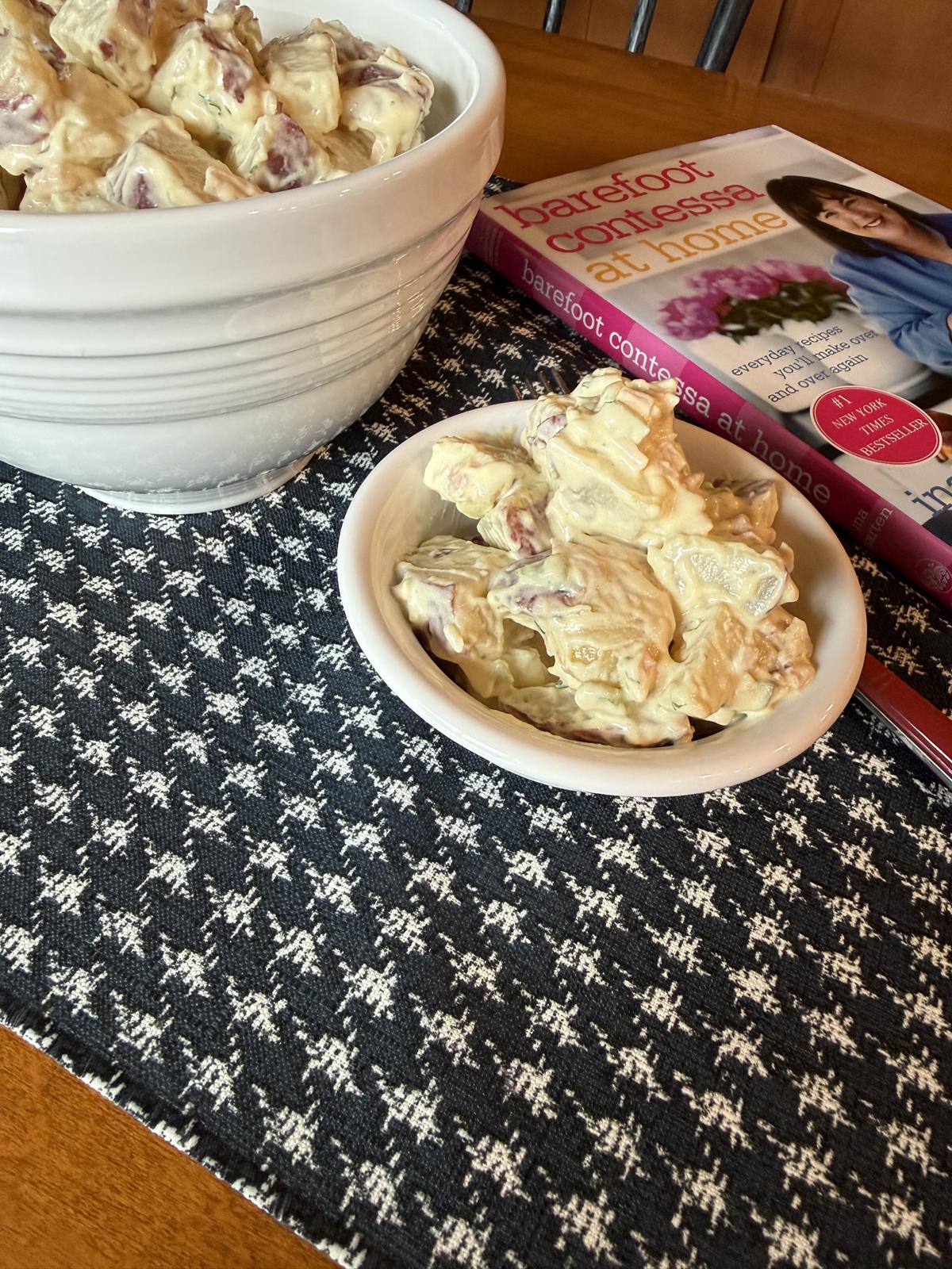 old fashioned potato salad in white bowl on table with cookbook in background