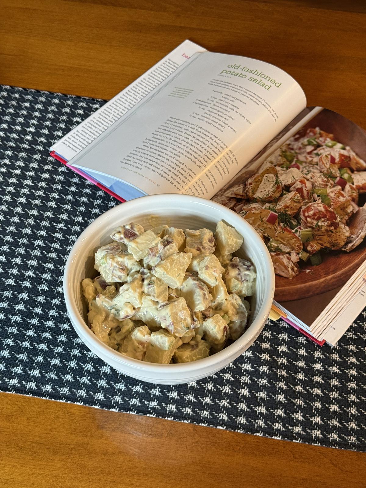 potato salad in white bowl with cookbook in background