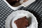 gluten free fudge brownie on white plate with pan of brownies in background
