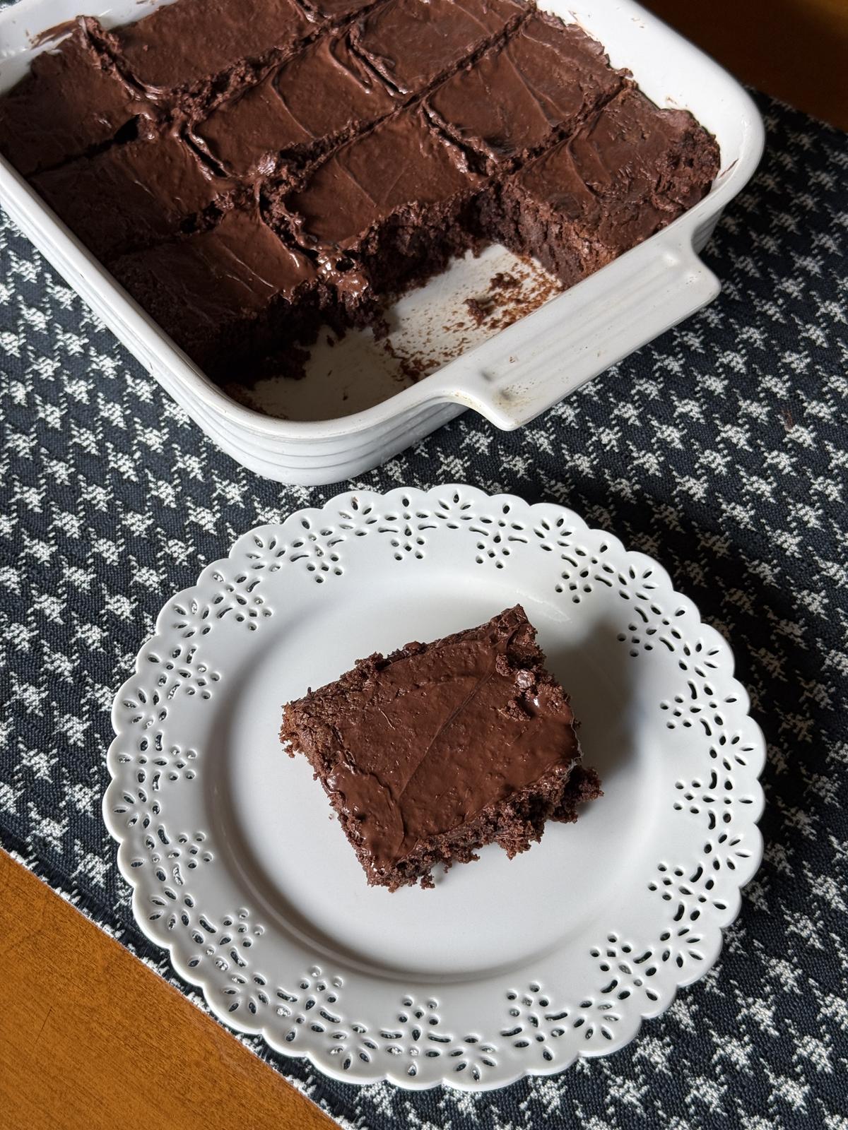 gluten free fudge brownie on white plate with pan of brownies in background