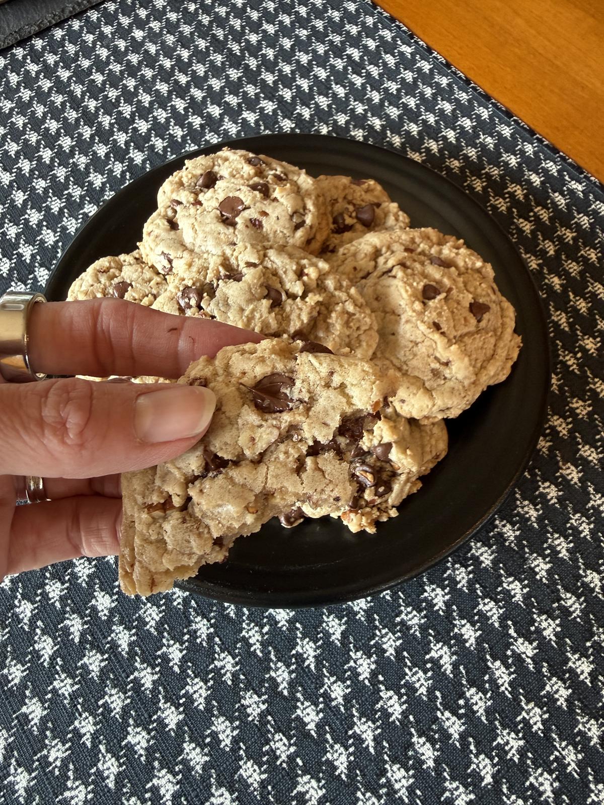 hand holding chocolate toffee pecan cookies and more cookies on black plate in background