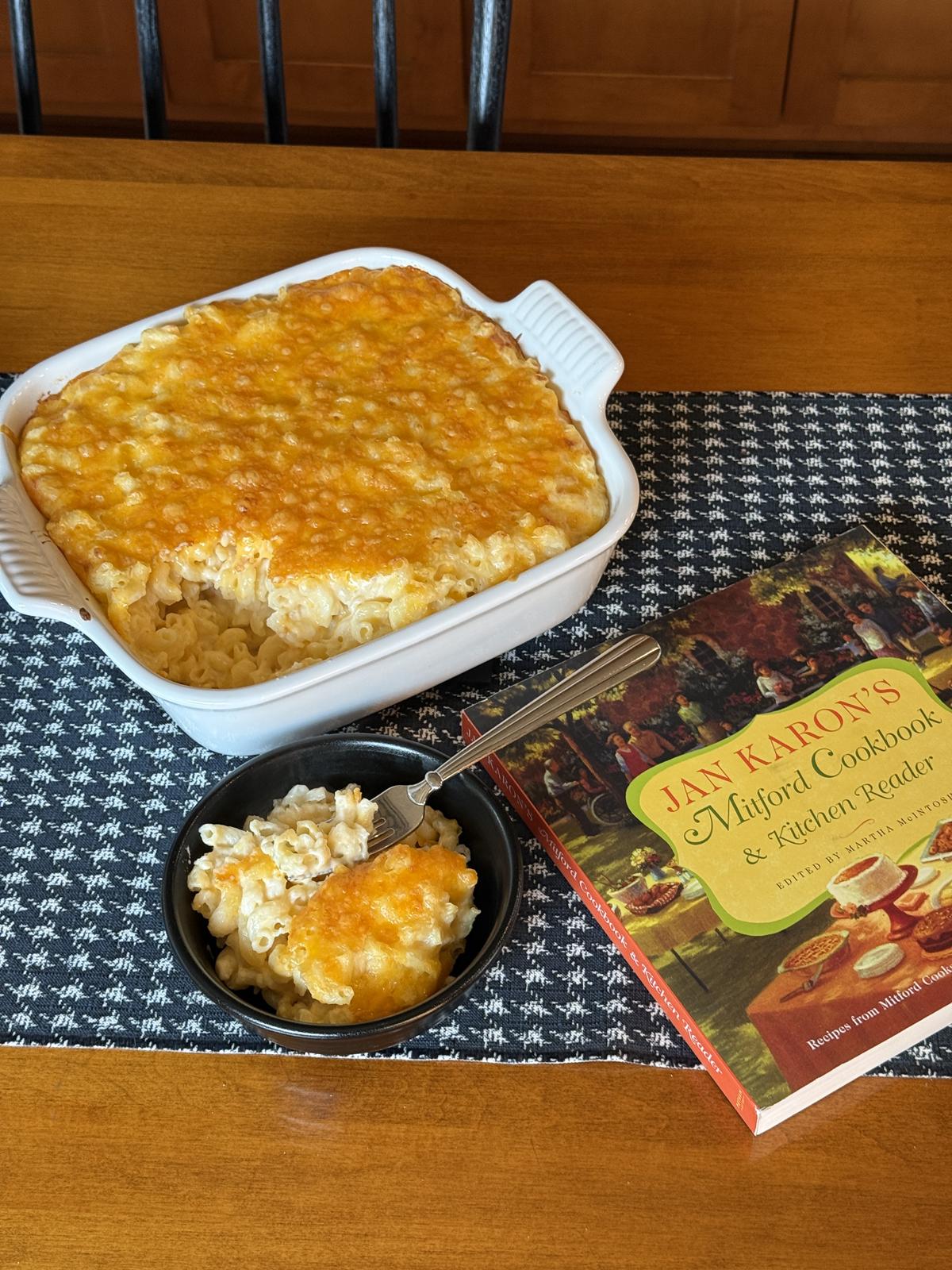 mac and cheese in a black bowl, a white casserole dish and The Mitford cookbook on table