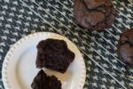 gluten free chocolate banana muffin on white plate with cooling rack with muffins on back