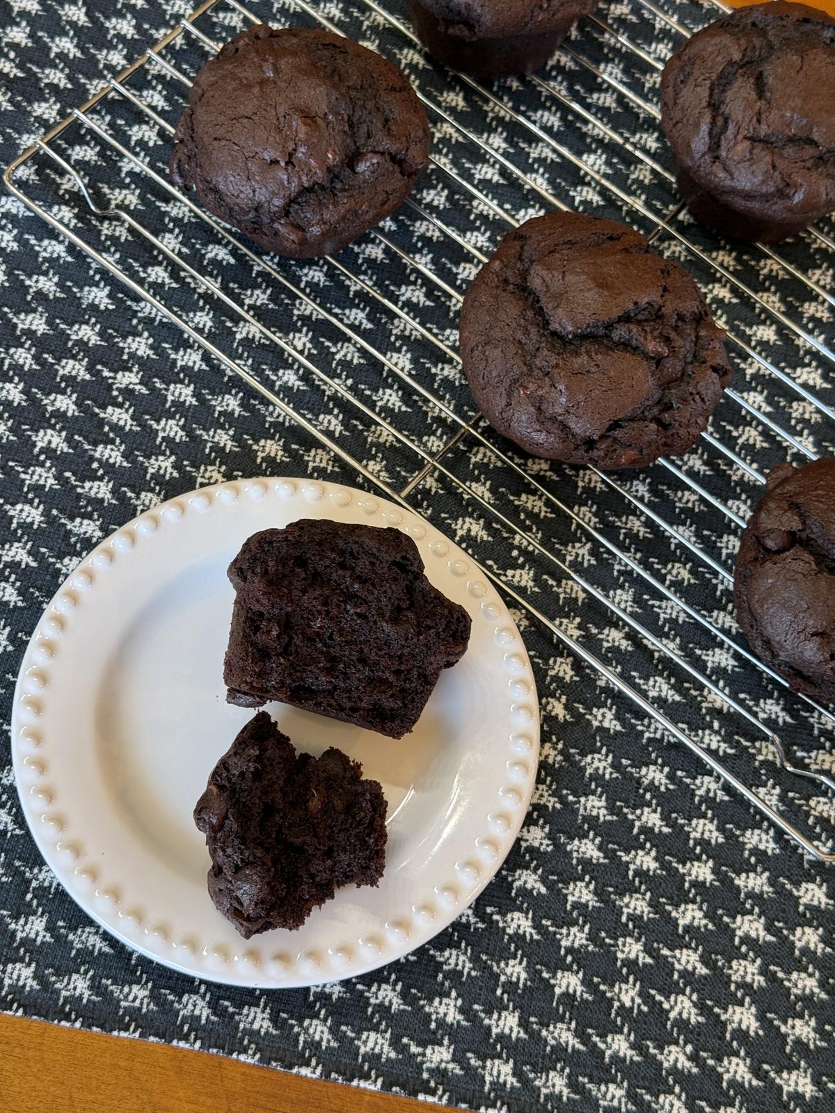 gluten free chocolate banana muffin on white plate with cooling rack with muffins on back