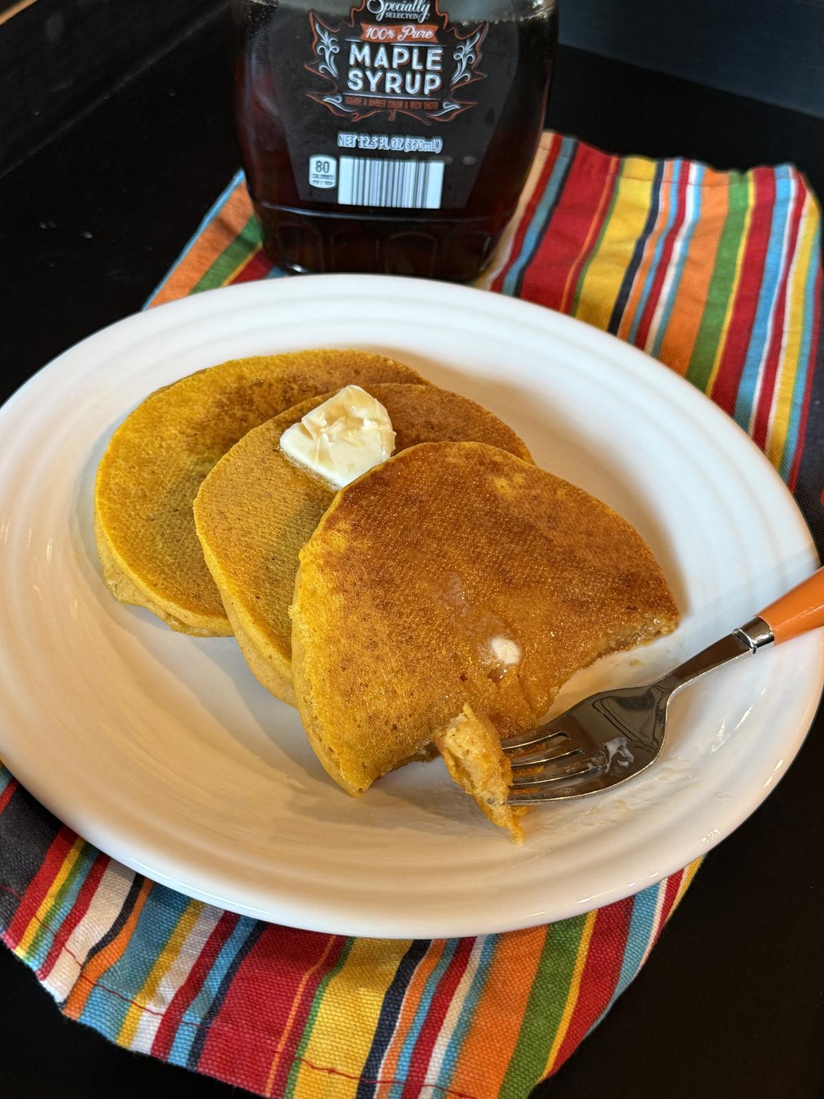 Homemade Gluten Free Ihop Pumpkin Pancakes on white plate with butter and syrup striped napkin in the background