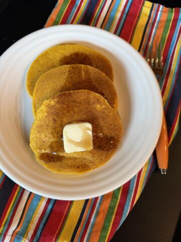 gluten free pumpkin pancakes with butter on white plate and striped napkin