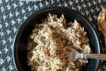 Homemade Rice A Roni with Ground Beef in black bowl with fork and white pan full of Rice A Roni on black and white table cloth