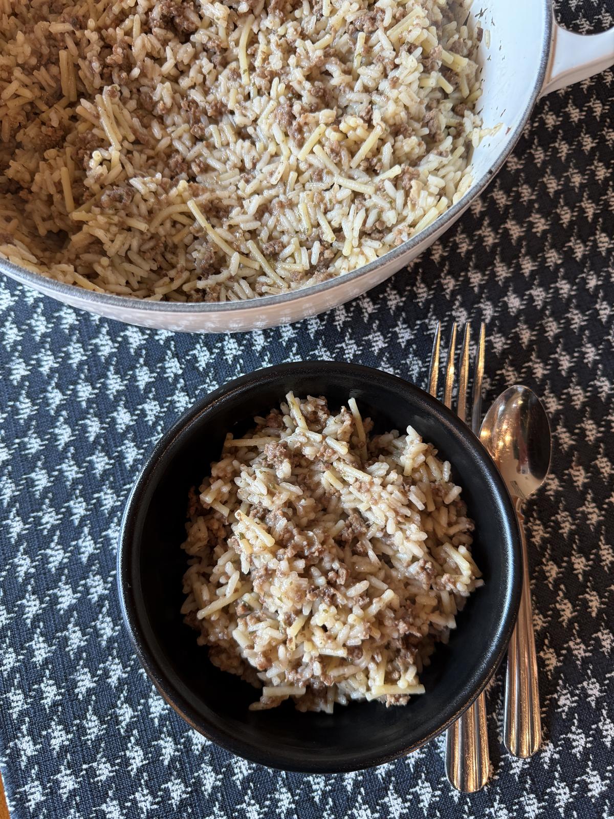 Homemade Rice A Roni with Ground Beef in black bowl and white pan full of Rice A Roni on black and white table cloth